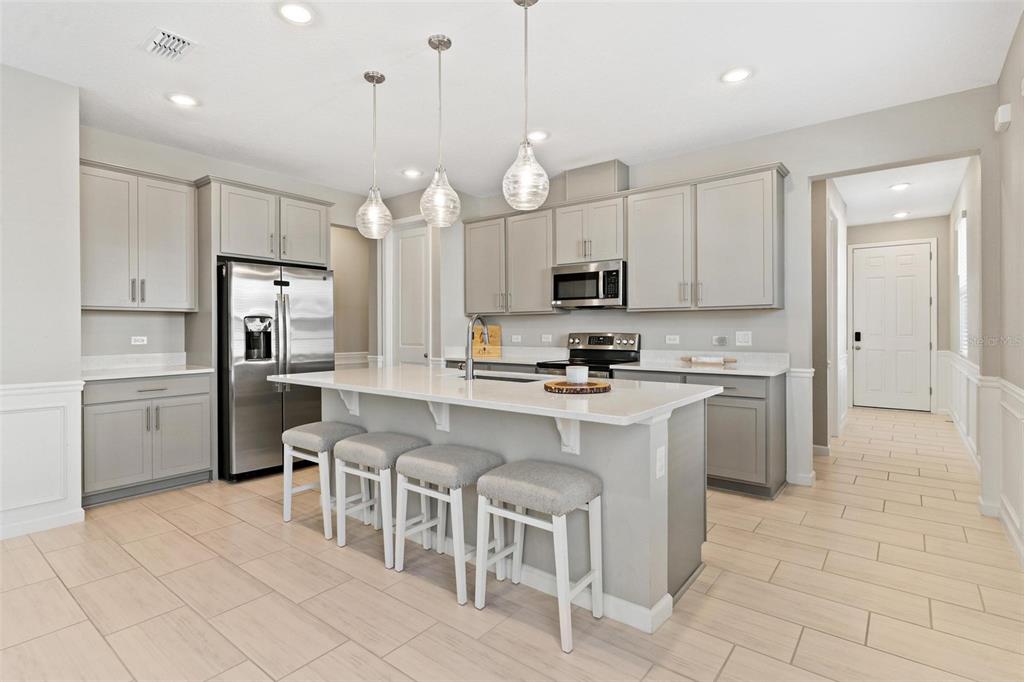 A modern kitchen features gray cabinets, stainless steel appliances, a white island, and tile flooring — 31788 BROADWATER AVENUE, LEESBURG, FL
