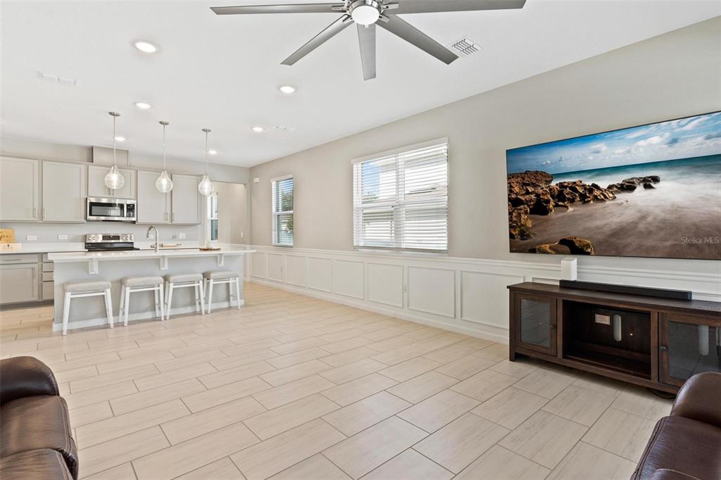 An open-concept living room and kitchen featuring light tile flooring, white wainscoting, and a ceiling fan — 31788 BROADWATER AVENUE, LEESBURG, FL