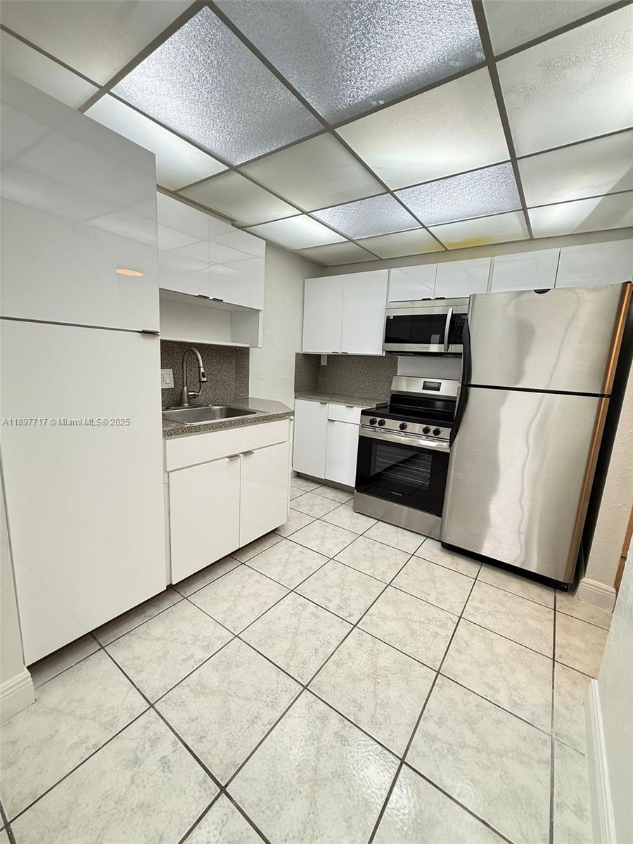 A kitchen features white cabinets, stainless steel appliances, and light-colored tiled flooring — 13499 Biscayne Blvd # 811, North Miami FL 33181, NORTH MIAMI, FL