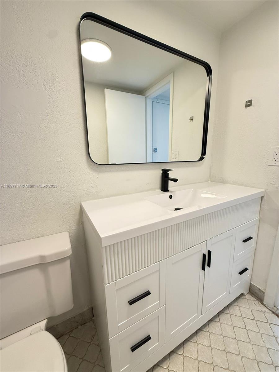 A bathroom features a white vanity with black hardware, a black-framed mirror, and patterned flooring — 13499 Biscayne Blvd # 811, North Miami FL 33181, NORTH MIAMI, FL
