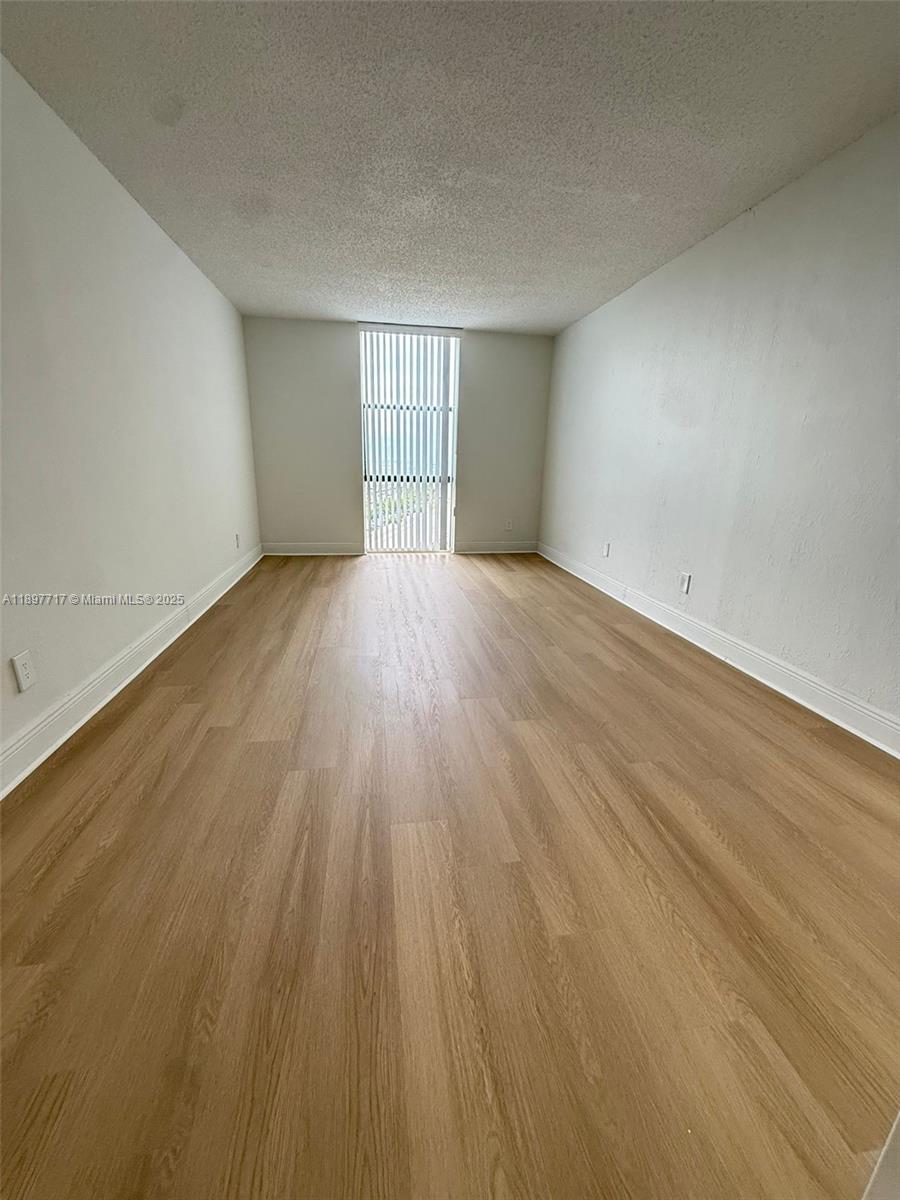 An empty room features light wood-look flooring, white walls, and a vertical blind window — 13499 Biscayne Blvd # 811, North Miami FL 33181, NORTH MIAMI, FL