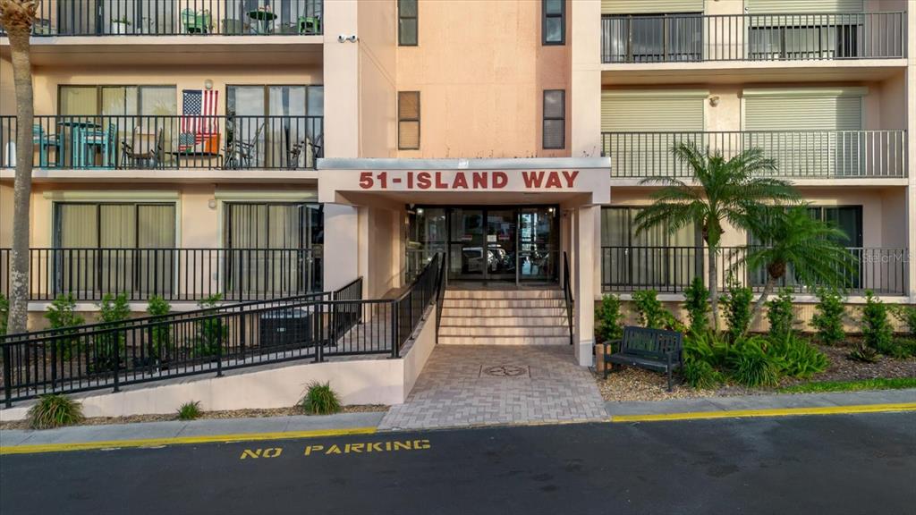 The exterior of a multi-story apartment building features a central entrance with stairs and ramp — 51 ISLAND WAY UNIT 801, CLEARWATER BEACH, FL