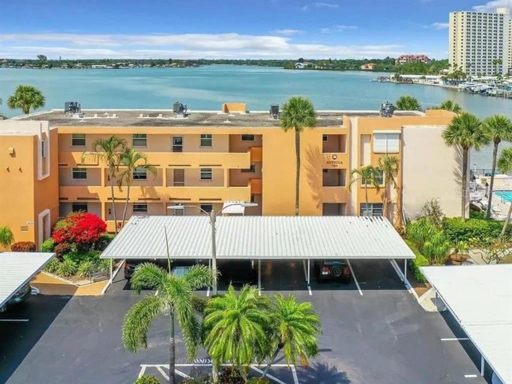 An exterior view of a multi-story apartment building with a covered parking area and water — 7560 BAY ISLAND DRIVE S UNIT 149, SOUTH PASADENA, FL