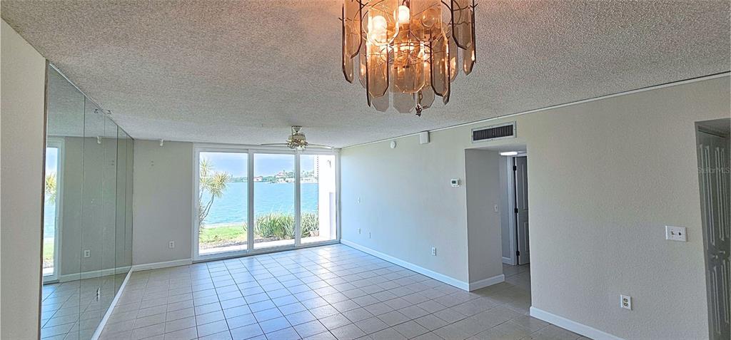 A living room features tile flooring, a mirrored wall, a chandelier, and sliding glass doors — 7560 BAY ISLAND DRIVE S UNIT 149, SOUTH PASADENA, FL
