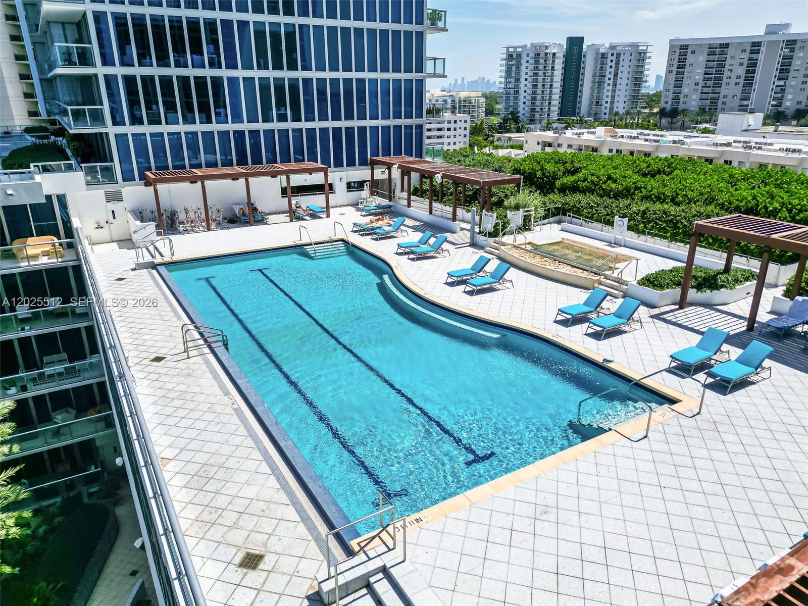 An elevated view of a rectangular swimming pool surrounded by lounge chairs and wooden pergolas — 6801 Collins Ave, Miami Beach FL 33141, MIAMI BEACH, FL