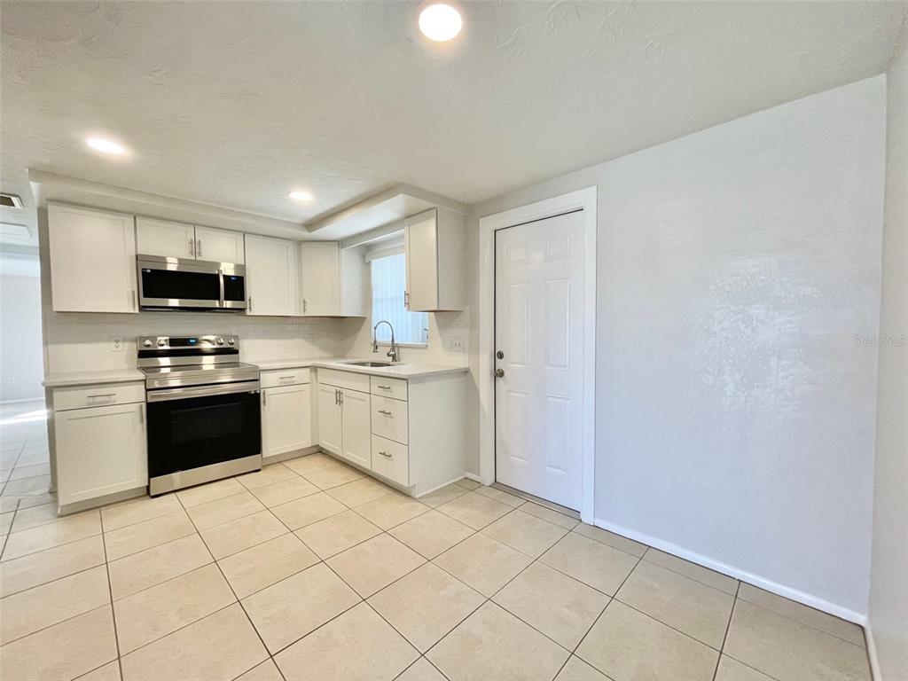 A kitchen with white cabinets, stainless steel appliances, and light-colored tile flooring — 5814 1ST AVENUE, NEW PORT RICHEY, FL