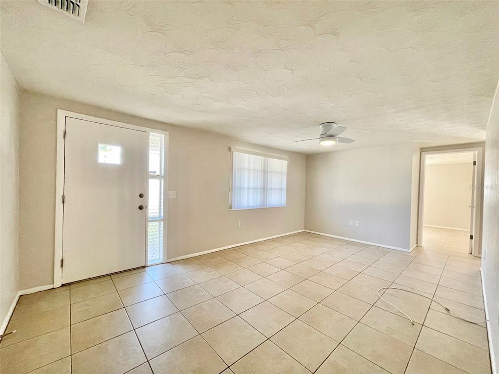 An empty living room features beige tile flooring, a ceiling fan, and a front door — 5814 1ST AVENUE, NEW PORT RICHEY, FL
