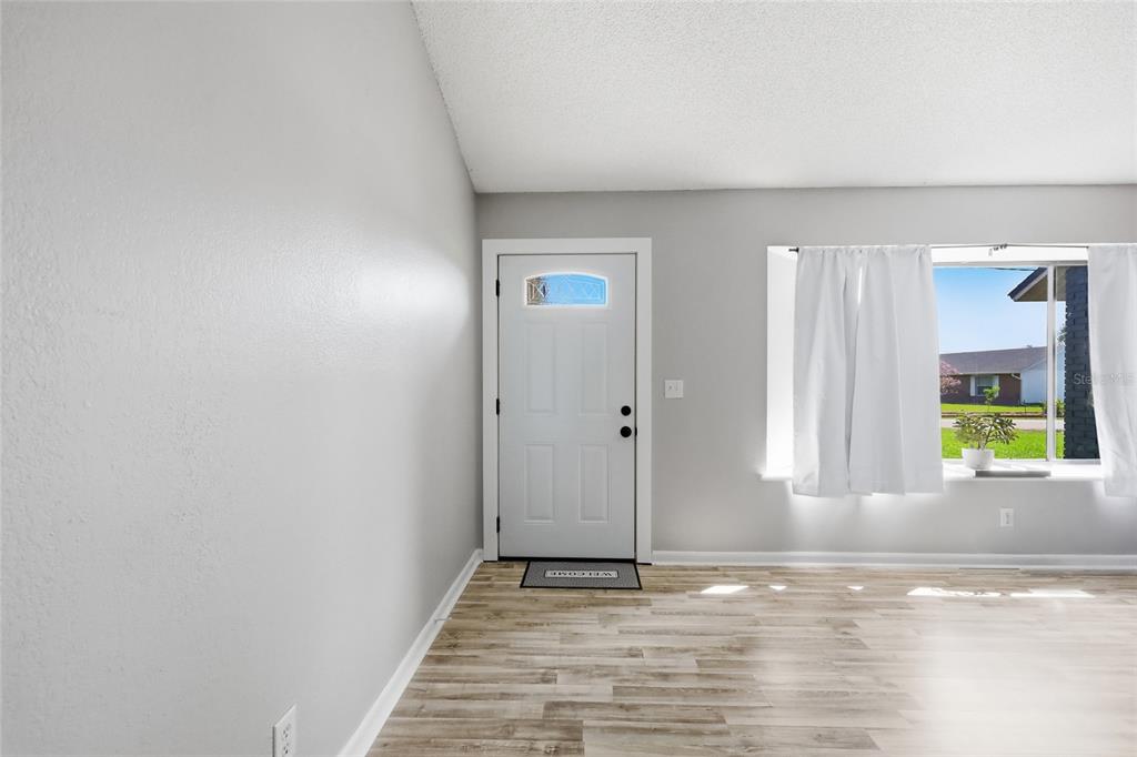 A bright entryway features light gray walls, wood-look flooring, a white front door, and windows — 2643 SALTERS COURT, DELTONA, FL