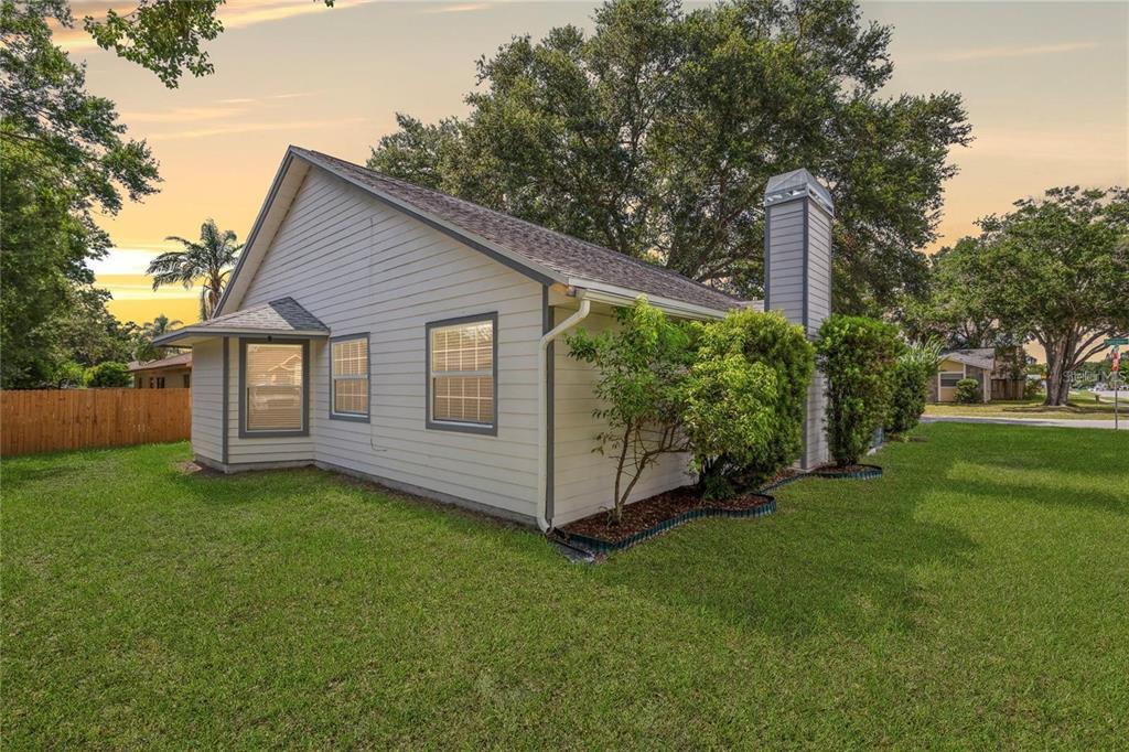 A side view of a single-story house with light siding, a chimney, and a lawn — 5116 PLANTATION DRIVE, HOLIDAY, FL