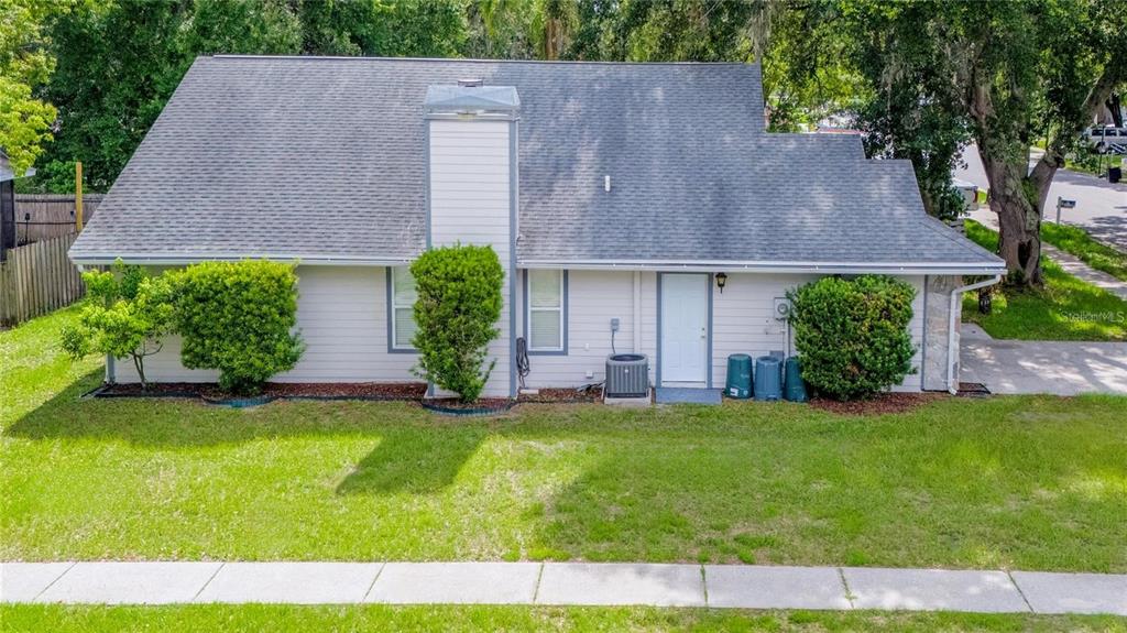 A side view of a light-colored house with a chimney, bushes, and a white door — 5116 PLANTATION DRIVE, HOLIDAY, FL