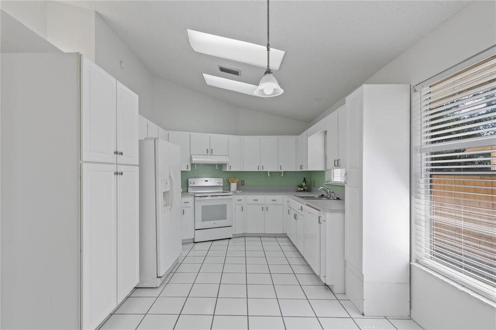 A white kitchen features white cabinets, a white refrigerator, a stove, and a tile floor — 5116 PLANTATION DRIVE, HOLIDAY, FL