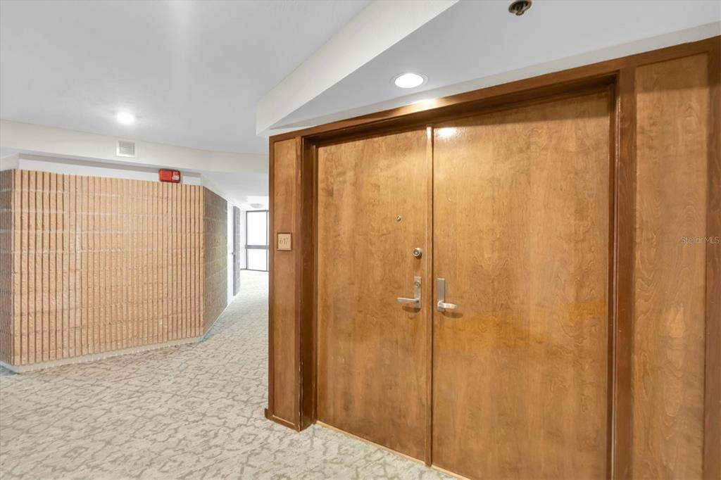 A hallway with patterned carpet leads to a double wooden door marked with number 617 — 1600 GULF BOULEVARD UNIT 617, CLEARWATER BEACH, FL