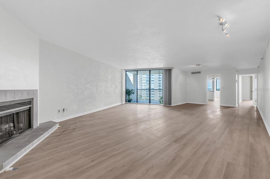 A spacious living room features light wood-look flooring, a fireplace, and a balcony with views — 1600 GULF BOULEVARD UNIT 617, CLEARWATER BEACH, FL
