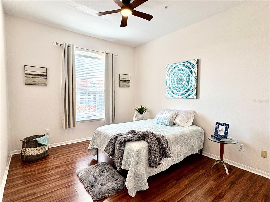 A bedroom features wood-look flooring, a ceiling fan, a window with curtains, and a bed — 18107 PEREGRINES PERCH PLACE UNIT 6303, LUTZ, FL