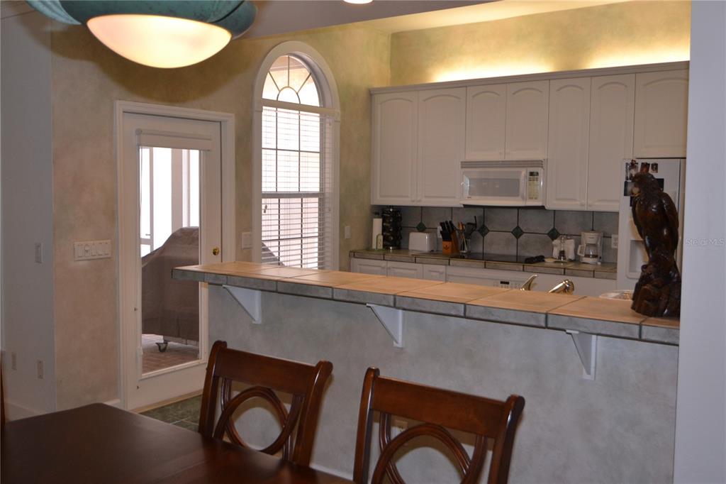 A kitchen with white cabinets, a tiled breakfast bar, and a glass door to outside — 79 NW 48TH BOULEVARD, GAINESVILLE, FL
