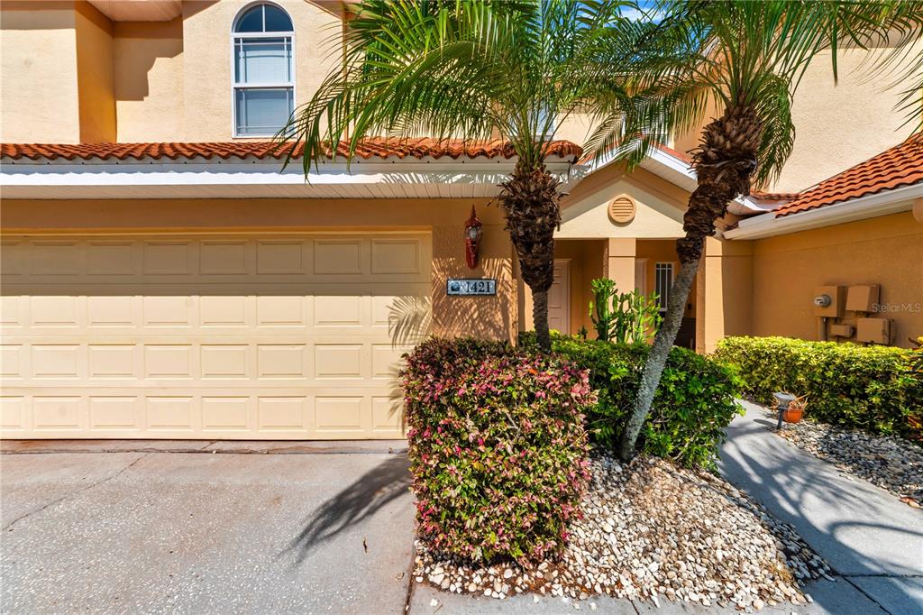 The exterior of a tan two-story townhouse features a garage, palm trees, and landscaping — 1421 RIDGE TERRACE, TARPON SPRINGS, FL