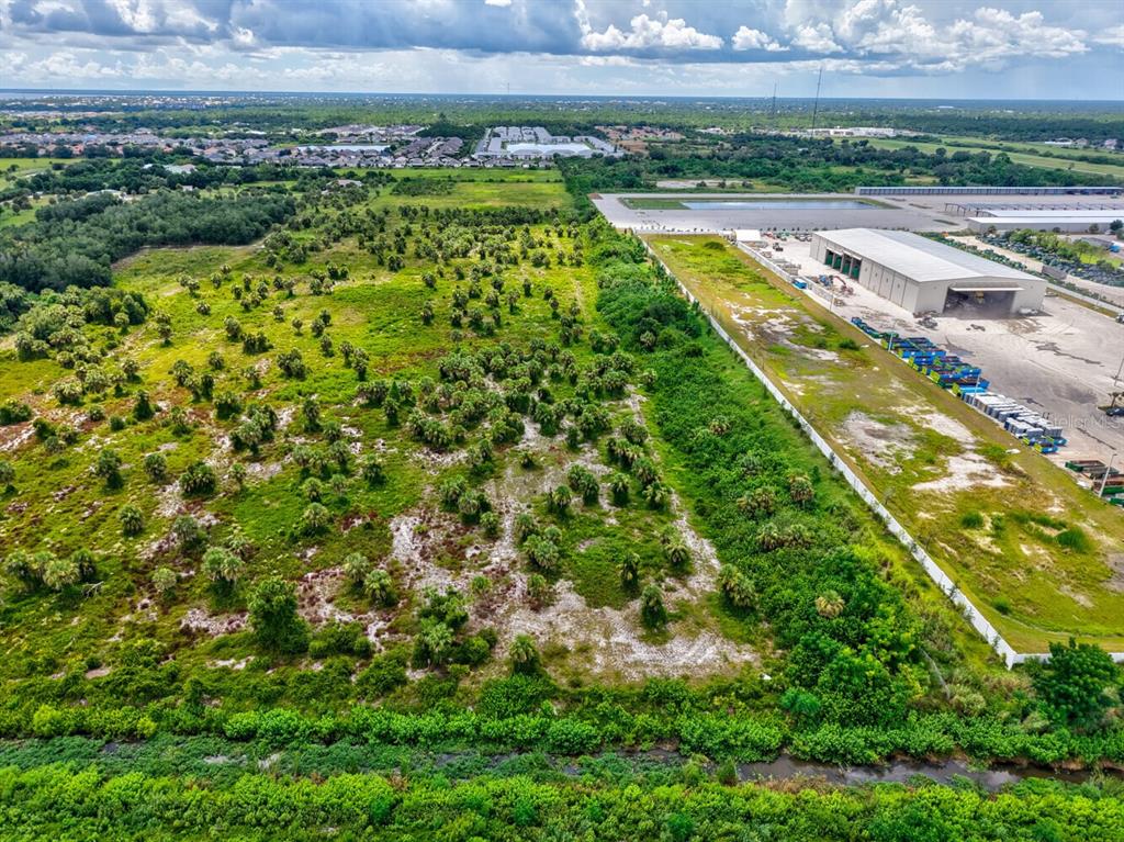 An aerial view shows a vacant, brush-covered lot adjacent to a large industrial warehouse building — 3285 ROWLAND DRIVE UNIT Tract G, PUNTA GORDA, FL