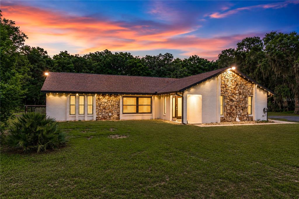 A single-story house with stone accents and a large lawn under a sunset sky — 2735 NE 127TH PLACE, ANTHONY, FL