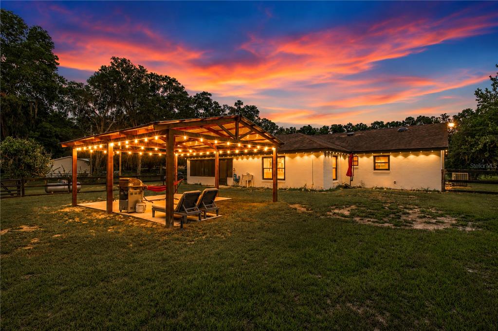 A backyard view of a house with a wooden pergola, string lights, and sunset sky — 2735 NE 127TH PLACE, ANTHONY, FL