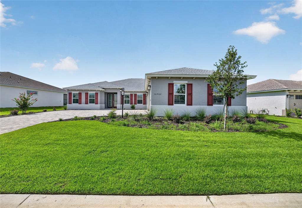 A single-story house with gray stucco walls, red shutters, and a paved driveway — 10202 SW 84TH STREET ROAD, OCALA, FL