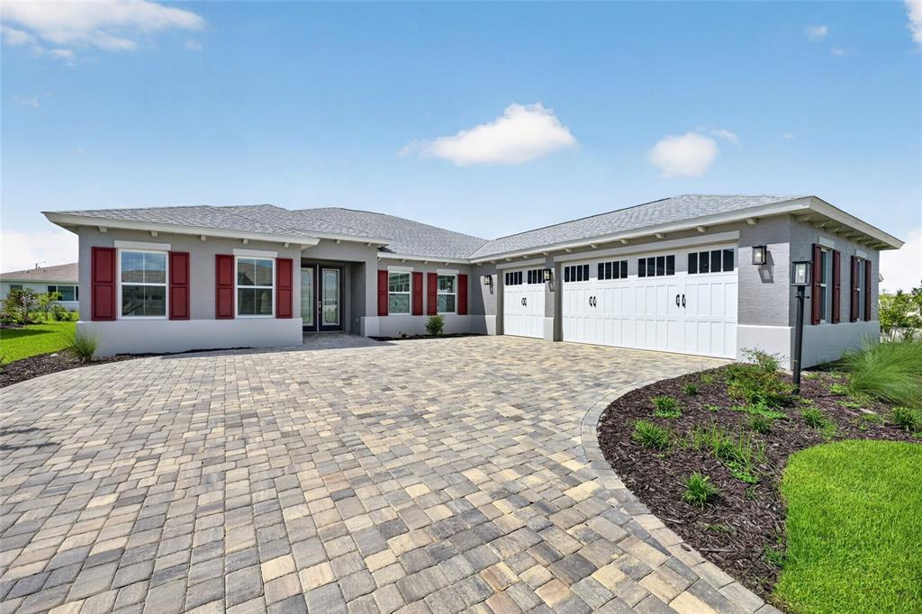 A single-story house with a gray stucco exterior, red shutters, and a paver driveway — 10202 SW 84TH STREET ROAD, OCALA, FL