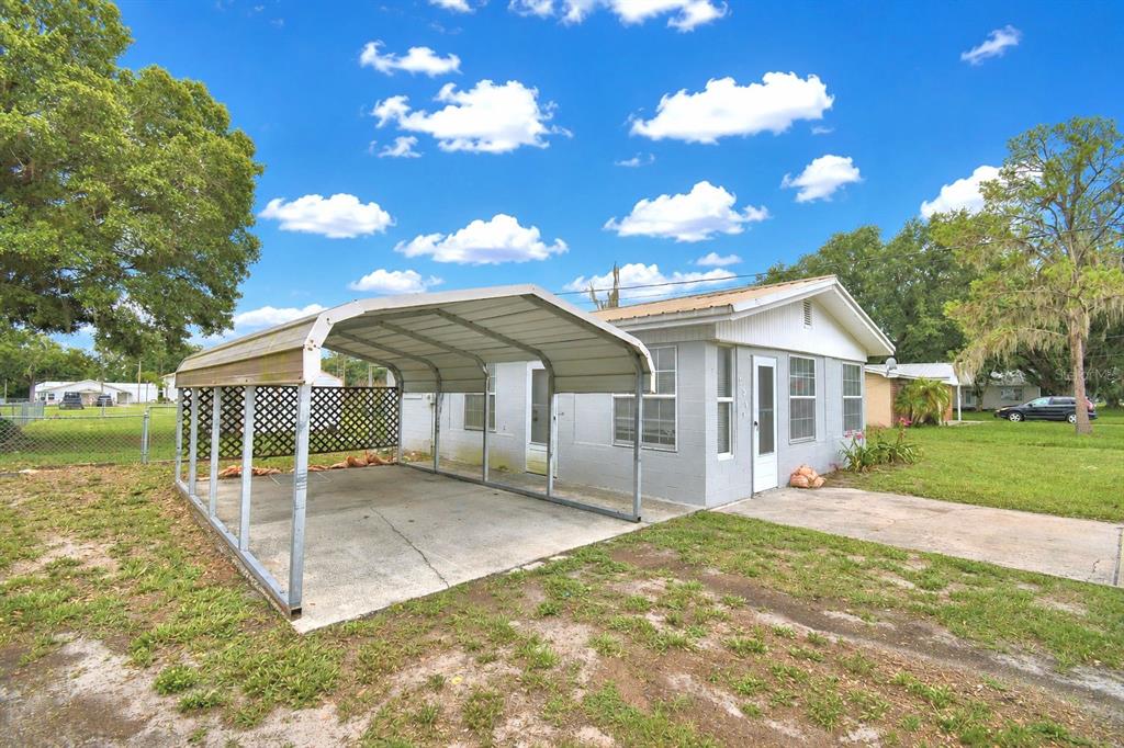 A gray one-story house with a metal carport and a concrete driveway under a blue sky — 906 N 9TH AVENUE, WAUCHULA, FL