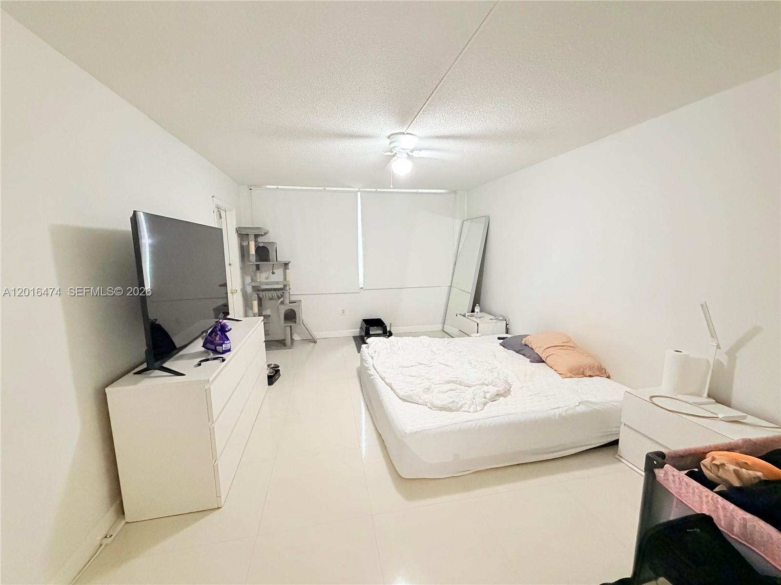 A bedroom features white walls, tile flooring, a bed on the floor, and a television — 1680 NE 191st St # 2, Miami FL 33179, MIAMI, FL