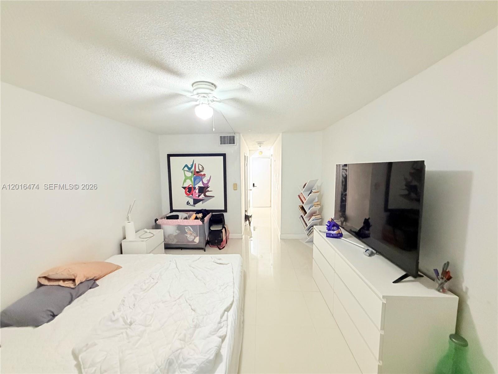 A bedroom features white tile floors, a bed, a dresser with a television, and artwork — 1680 NE 191st St # 2, Miami FL 33179, MIAMI, FL