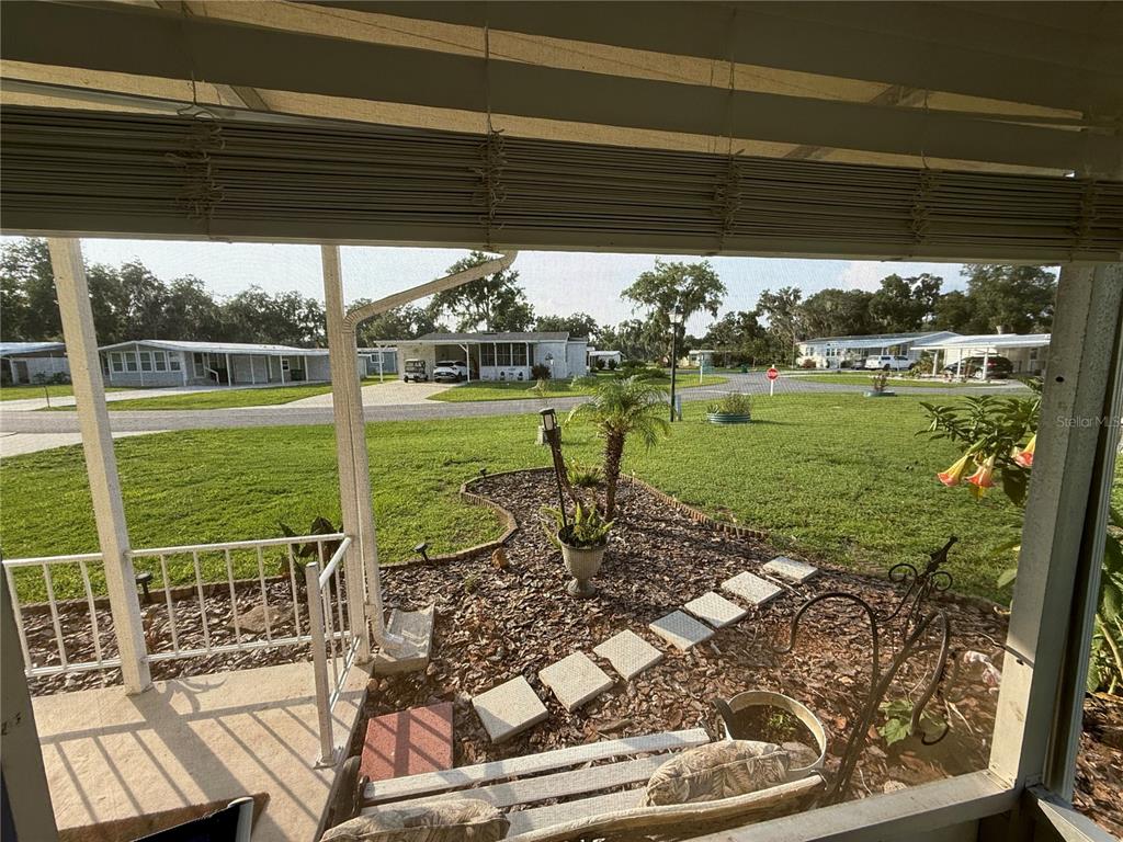 A view from a screened-in porch looking out over a grassy yard and neighboring houses — 48 S BOBWHITE ROAD, WILDWOOD, FL
