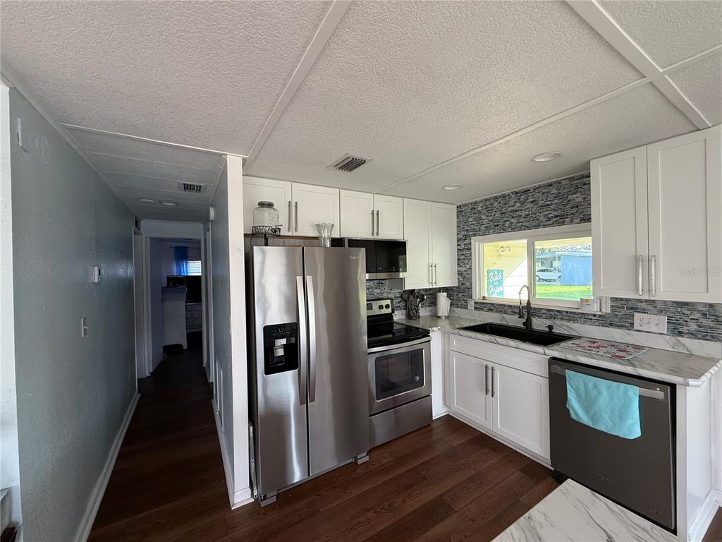 A kitchen features white cabinets, stainless steel appliances, a dark sink, and wood-look flooring — 48 S BOBWHITE ROAD, WILDWOOD, FL