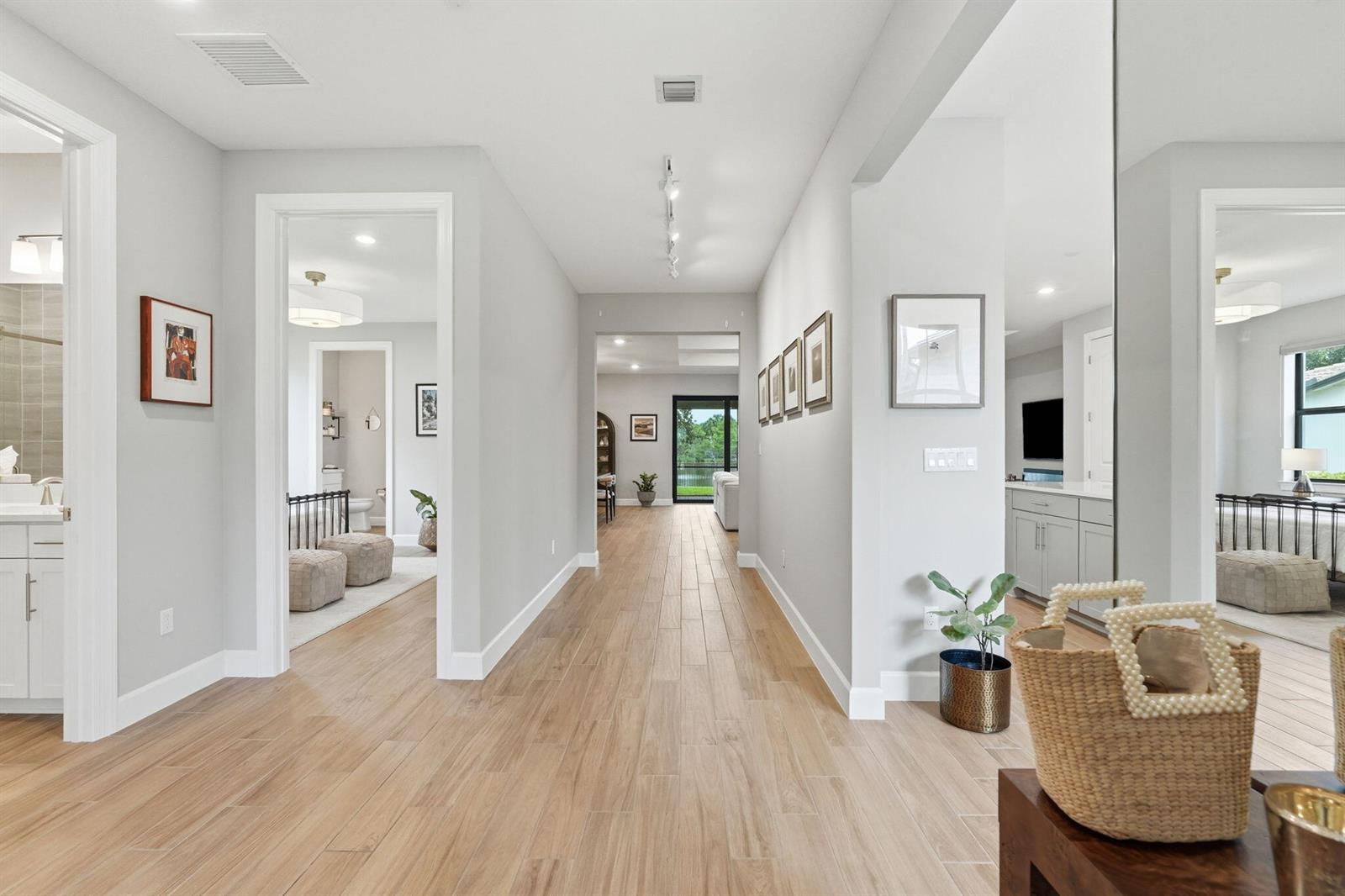A hallway with light wood-look tile flooring leads toward a glass door and outdoor view — 208 Sonoma Isles Circle, Jupiter FL 33478, JUPITER, FL
