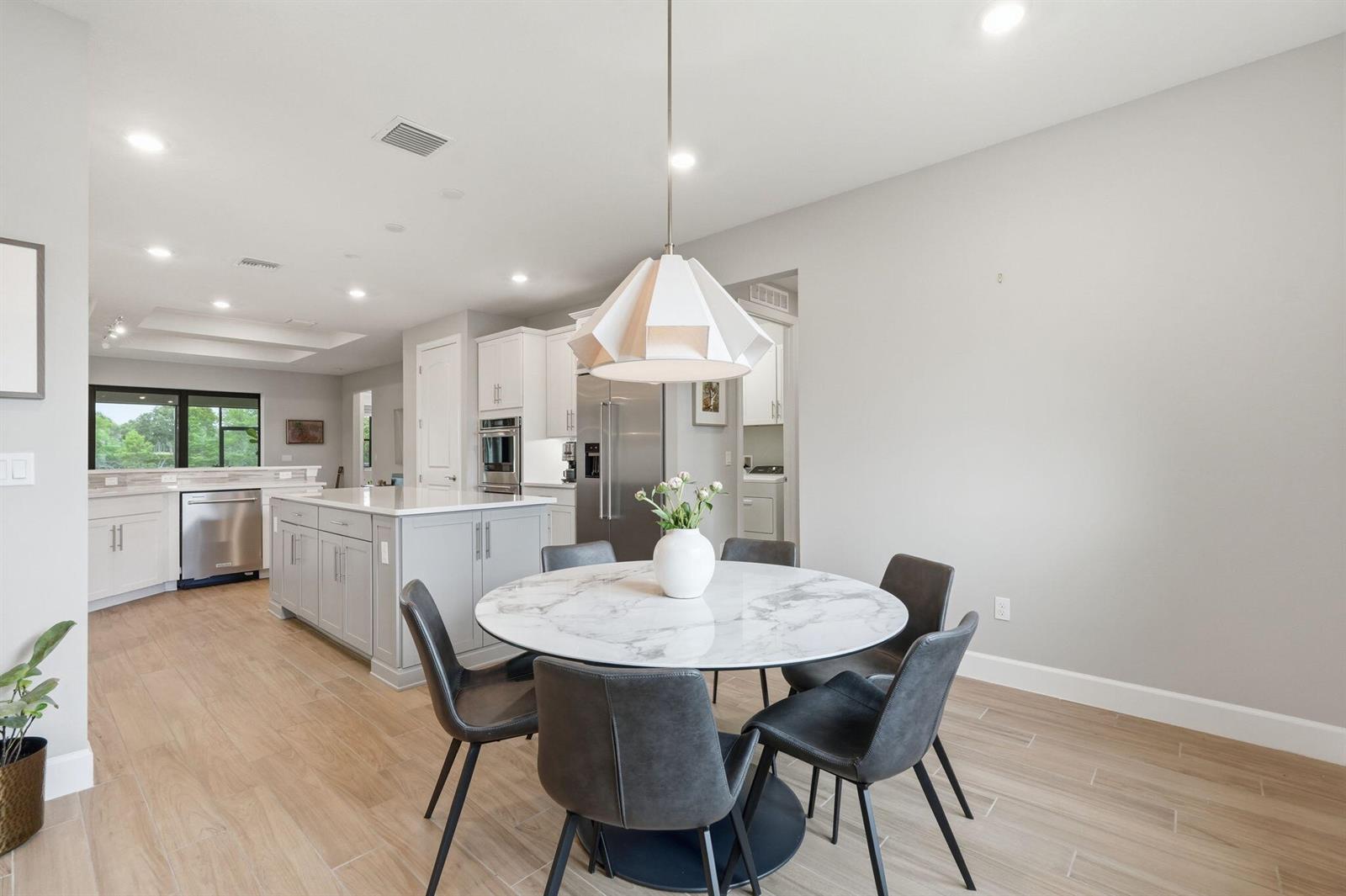 A dining area with a marble-topped table and gray chairs sits before an open kitchen — 208 Sonoma Isles Circle, Jupiter FL 33478, JUPITER, FL
