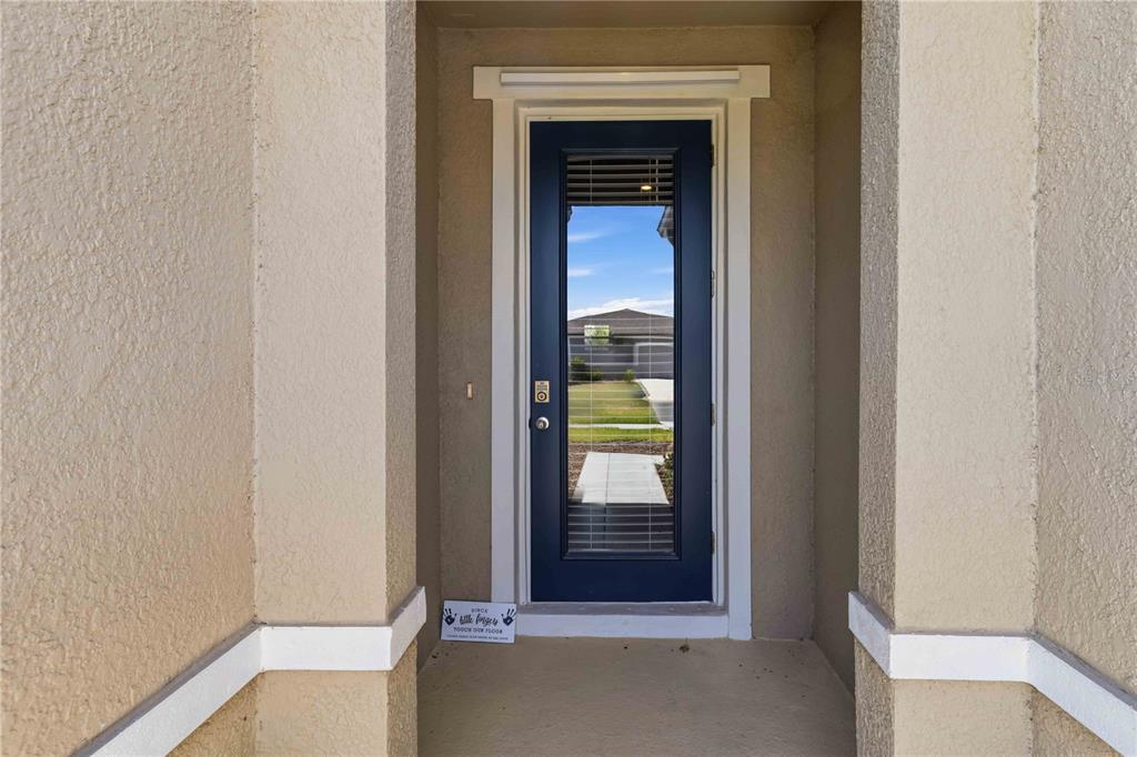 A dark blue front door with a glass insert is set within a covered entryway — 10009 DAYBREAK GLEN, PARRISH, FL