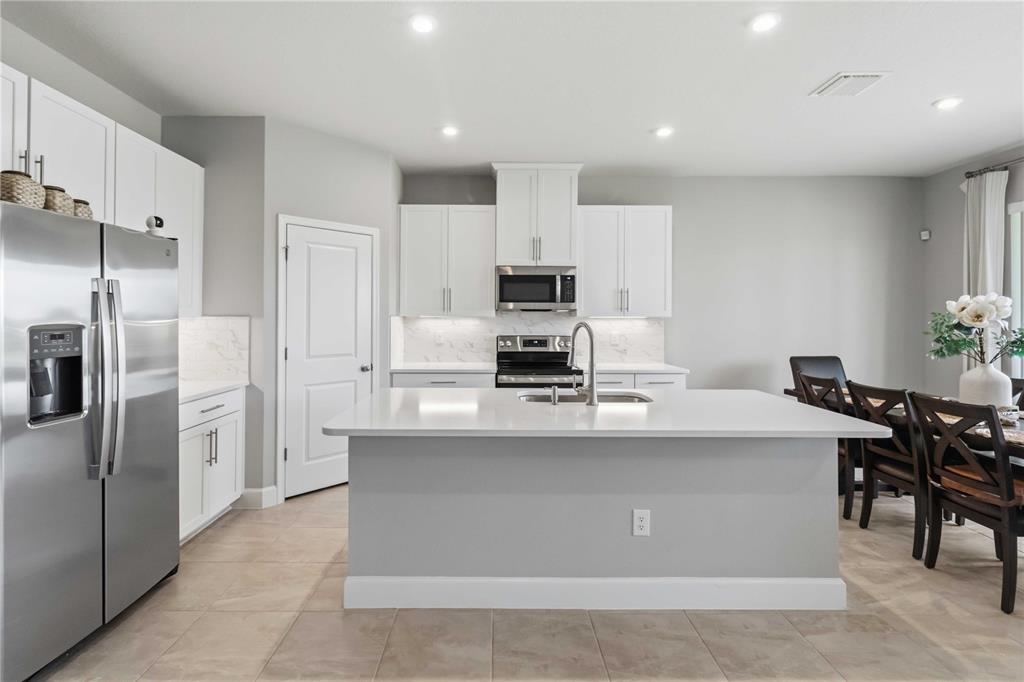 A modern kitchen features white cabinets, stainless steel appliances, a center island, and tile flooring — 10009 DAYBREAK GLEN, PARRISH, FL