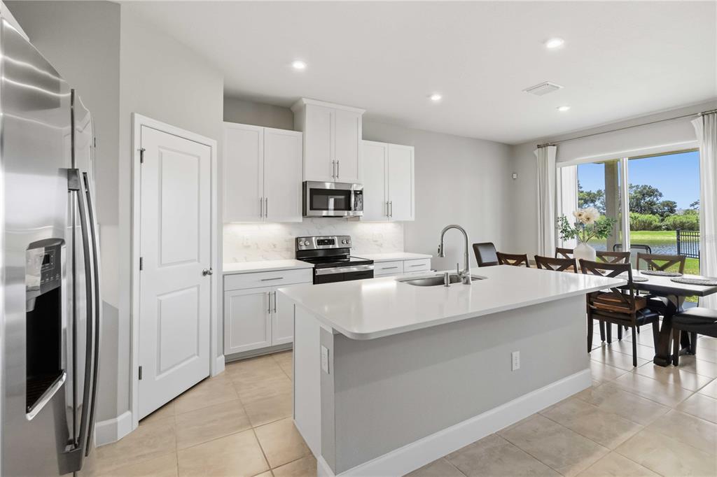 A modern kitchen features white cabinets, a central island, stainless appliances, and a dining area — 10009 DAYBREAK GLEN, PARRISH, FL