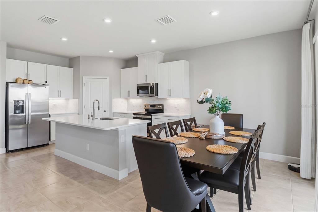 A modern kitchen with white cabinets and a dining area featuring a dark wood table — 10009 DAYBREAK GLEN, PARRISH, FL