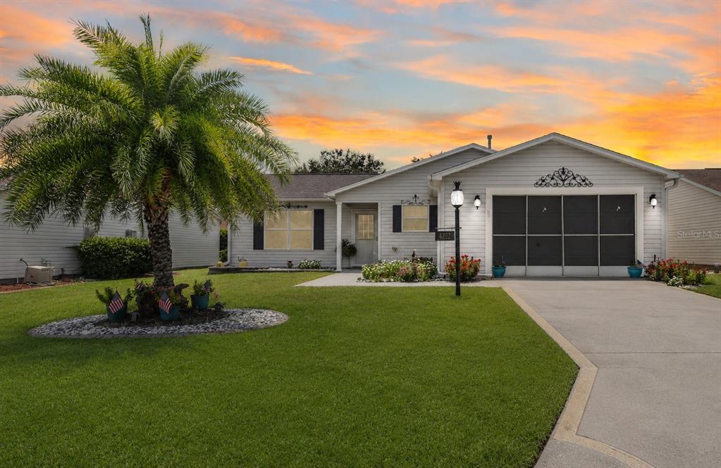 A single-story house with light siding, a palm tree, and a concrete driveway at sunset — 3448 JACONA PLACE, THE VILLAGES, FL