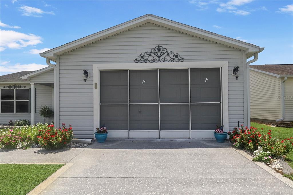 The exterior of a house features a garage with a sliding screen door and landscaping — 3448 JACONA PLACE, THE VILLAGES, FL