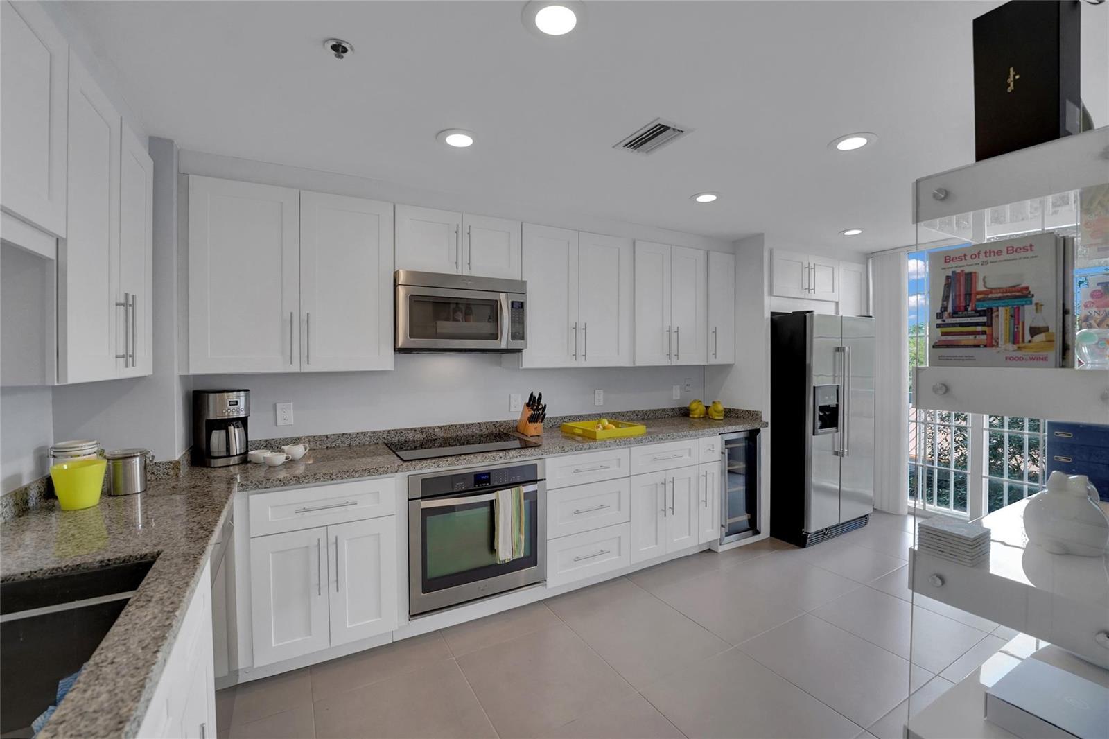A modern kitchen features white cabinetry, granite countertops, stainless steel appliances, and large floor tiles — 4108 W Palm Aire Drive # 083b, Pompano Beach FL 33069, POMPANO BEACH, FL