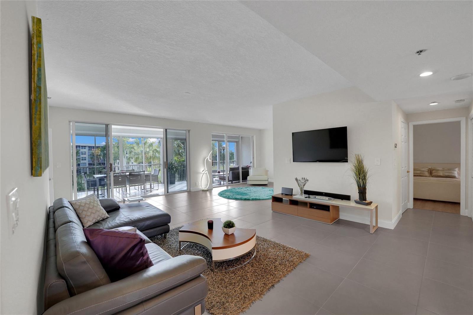 A living room features gray tile flooring, a leather sectional, and sliding glass doors to balconies — 4108 W Palm Aire Drive # 083b, Pompano Beach FL 33069, POMPANO BEACH, FL