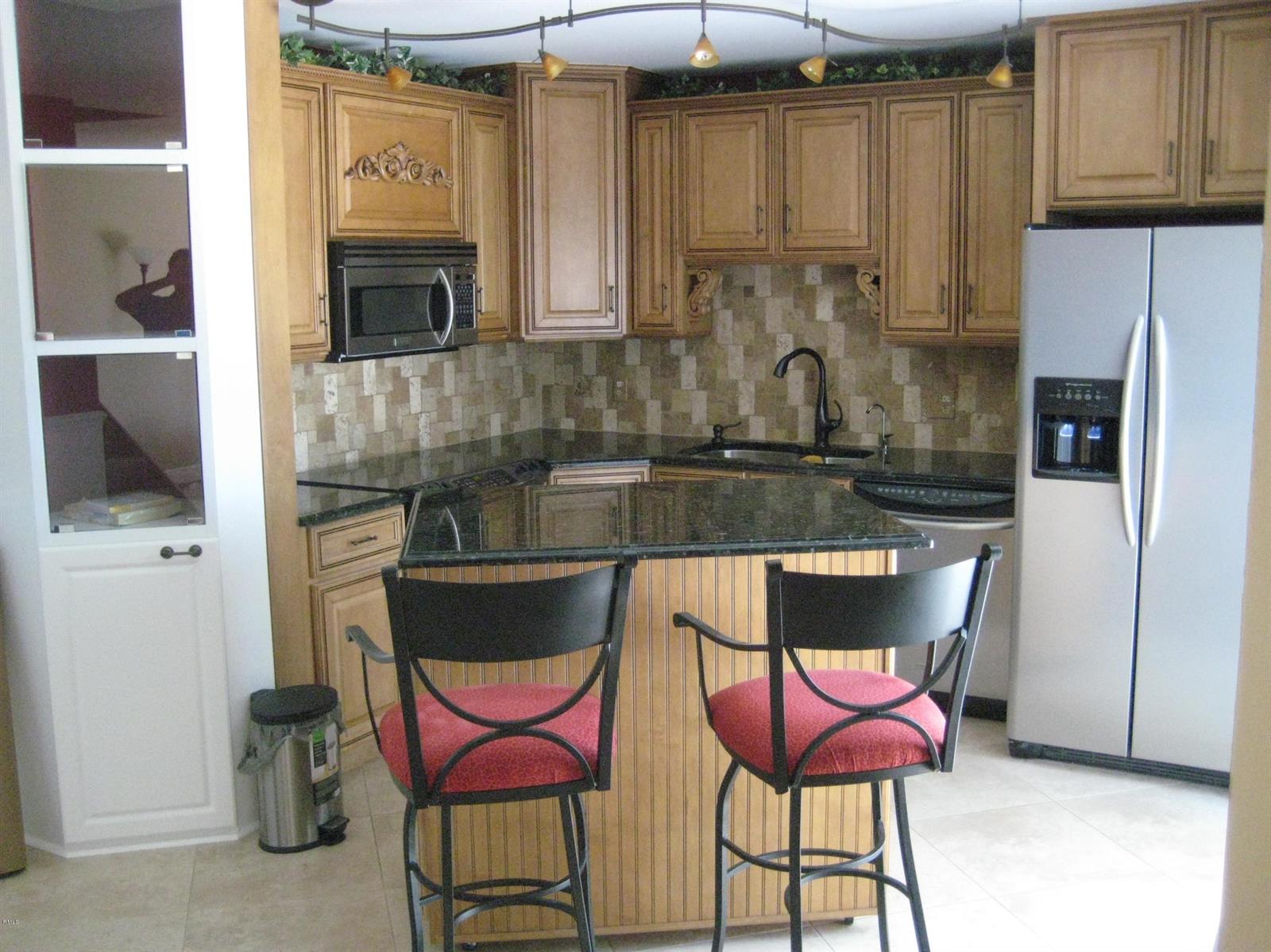 A kitchen features wood cabinets, granite countertops, a center island with bar stools, and appliances — 3900 SE County Line Road # 24d, Tequesta FL 33469, TEQUESTA, FL
