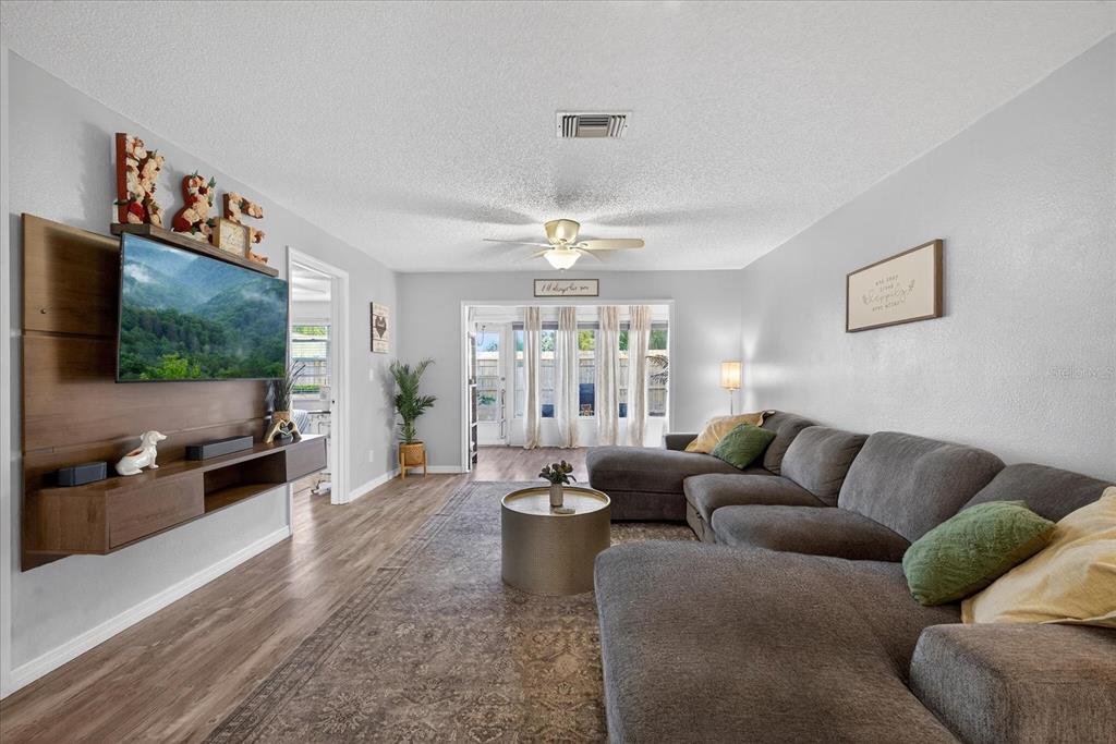 A living room features a gray sectional sofa, a wall-mounted television, and wood-look flooring — 3230 TEESIDE DRIVE, NEW PORT RICHEY, FL