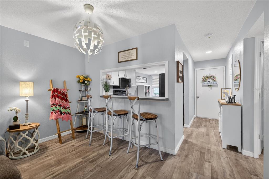 A dining area features a breakfast bar, three stools, wood-look flooring, and a modern light fixture — 3230 TEESIDE DRIVE, NEW PORT RICHEY, FL