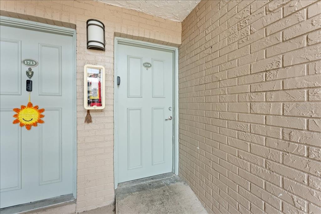 Two light-colored doors with unit numbers are set into a beige brick exterior wall — 7210 N MANHATTAN AVENUE UNIT 1714, TAMPA, FL