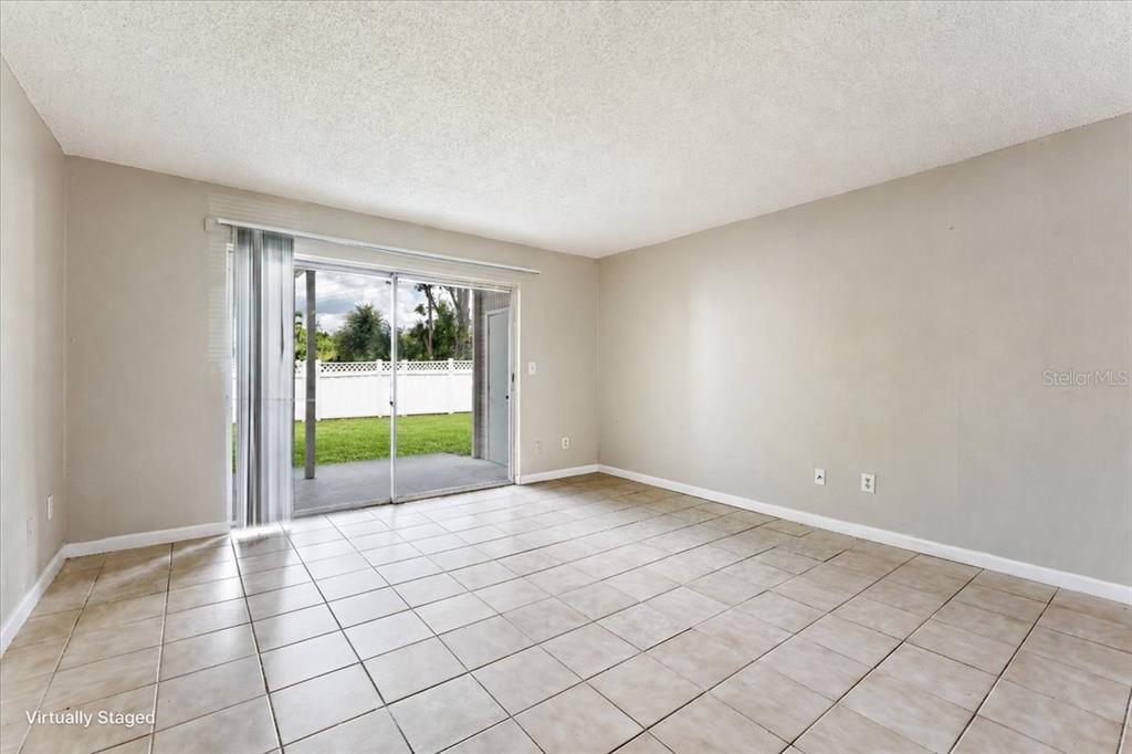 An empty living room features beige tile flooring, light-colored walls, and a sliding glass door — 7210 N MANHATTAN AVENUE UNIT 1714, TAMPA, FL