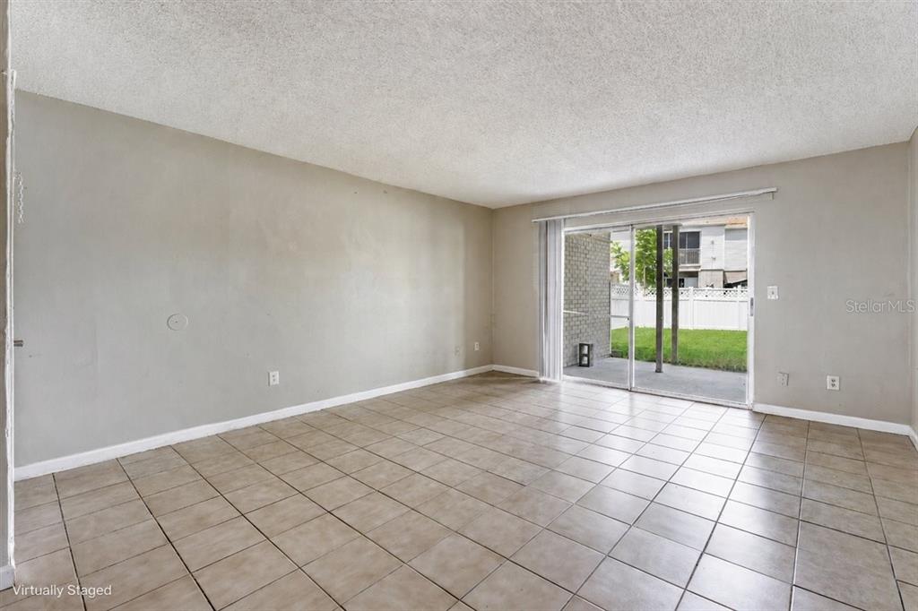 An empty room features beige tiled floors, light-colored walls, and a sliding glass door — 7210 N MANHATTAN AVENUE UNIT 1714, TAMPA, FL