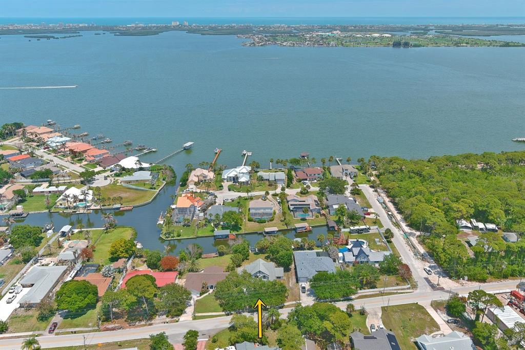 An aerial view shows a residential neighborhood with houses near a canal and a large bay — 2080 NEWFOUND HARBOR DRIVE, MERRITT ISLAND, FL