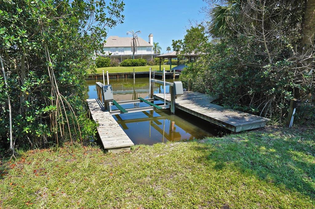 A wooden boat lift and dock sit on a canal surrounded by lush green vegetation — 2080 NEWFOUND HARBOR DRIVE, MERRITT ISLAND, FL