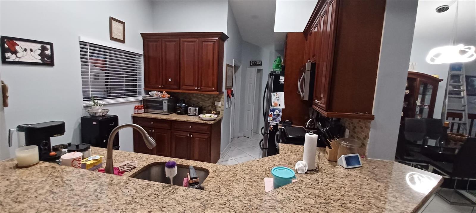 A kitchen features wood cabinets, granite countertops, a stainless steel sink, and a pantry door — 20 Via De Casas Sur # 204, Boynton Beach FL 33426, BOYNTON BEACH, FL