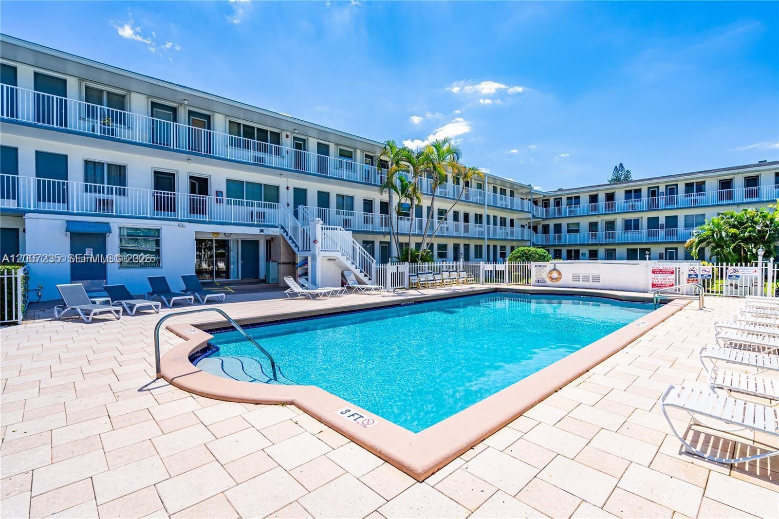 A swimming pool is surrounded by a paved deck and a multi-story apartment building — 15610 NE 6th Ave # 18C, Miami FL 33162, MIAMI, FL